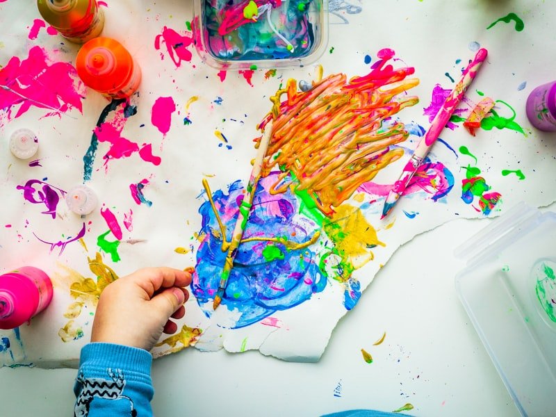 Top-down view of a child's hand painting colourful artwork at the kids' maker workshop
